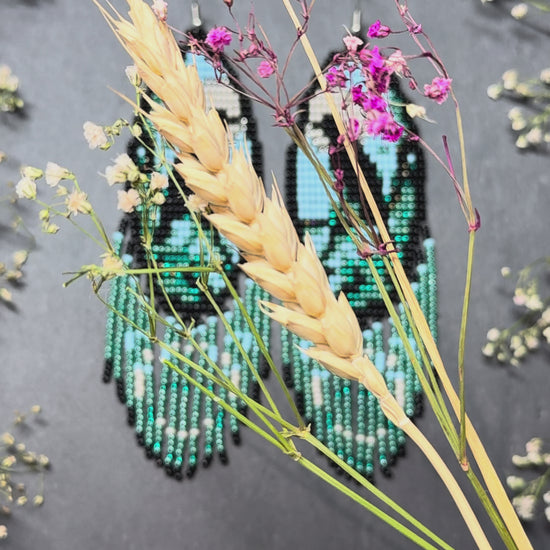 Long handmade beaded earrings in black, green, blue and beige featuring a raven and moon design with fringe. Boho statement jewelry, unique gift for her video 1
